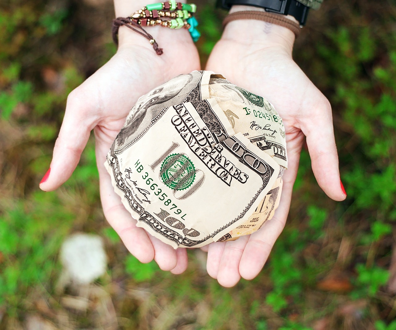 Two hands holding a ball of cash outwardly as a gift
